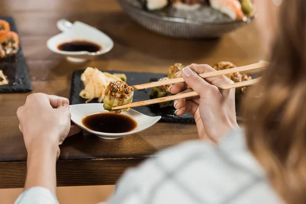 Teilansicht einer Frau, die im Restaurant Sushi mit Stäbchen in Sojasauce taucht — Stockfoto