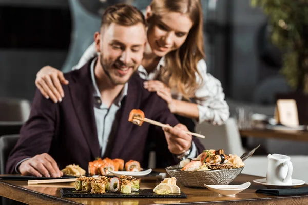 Happy attractive couple having dinner and eating tasty sushi rolls in restaurant — Stock Photo
