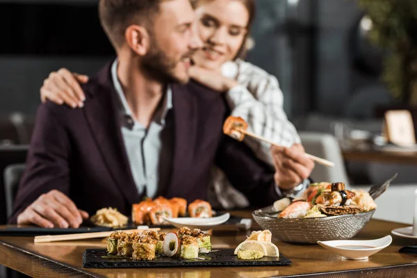 Pareja sonriente joven cenando y comiendo deliciosos rollos de sushi en el restaurante - foto de stock