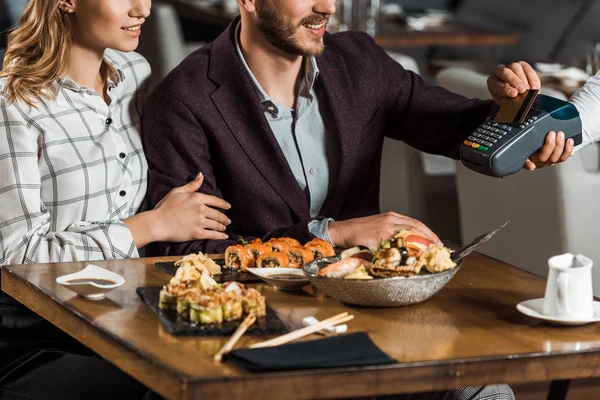 Teilansicht eines Paares, das am Tisch sitzt, während der Mann das Abendessen im Restaurant bezahlt — Stockfoto