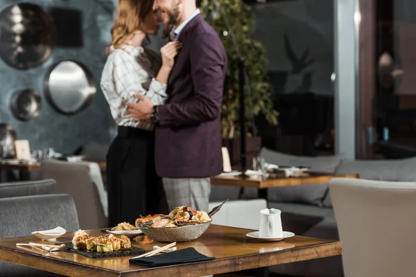 Vista parcial do belo casal abraço dançando atrás da mesa servida com sushi no restaurante — Fotografia de Stock