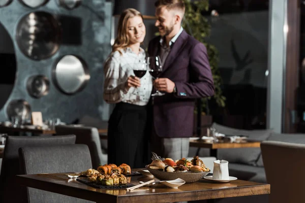 Vista cortada de casal atraente perto da mesa servida com sushi no restaurante — Fotografia de Stock