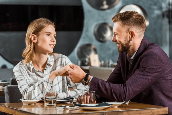Attraente giovane coppia adulta che si tiene per mano mentre si siede nel ristorante — Foto stock