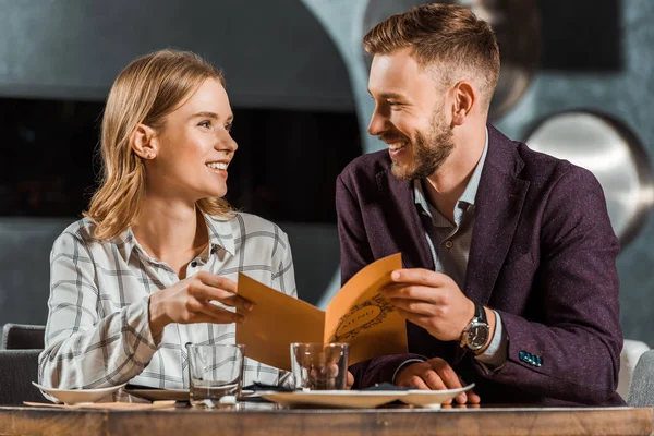 Casal encantador olhando um para o outro enquanto segurando menu no restaurante — Fotografia de Stock