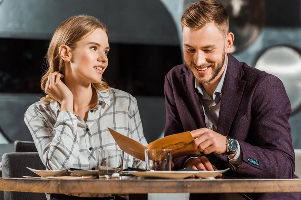 Happy smiling couple looking in menu to order dinner in restaurant — Stock Photo