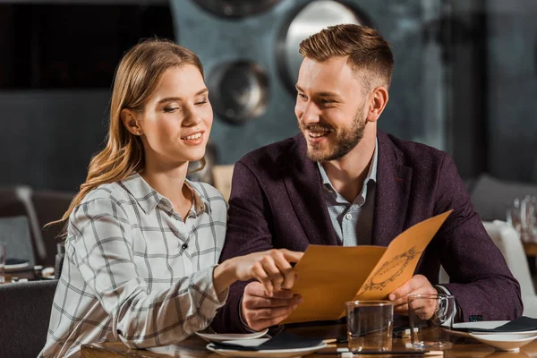 Frau zeigt auf etwas, während junges erwachsenes Paar in der Speisekarte sucht, um Abendessen im Restaurant zu bestellen — Stockfoto