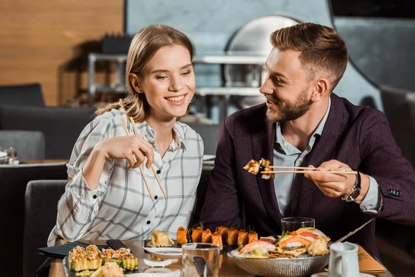 Attraente coppia sorridente mangiare insieme panini di sushi nel ristorante — Foto stock