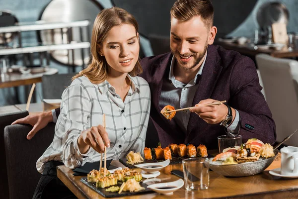 Happy smiling young adult couple eating sushi rolls in restaurant — Stock Photo