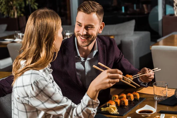 Belo casal feliz comer rolos de sushi no restaurante — Fotografia de Stock