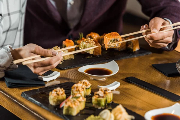 Cropped view of people eating sushi with chopsticks in restaurant — Stock Photo