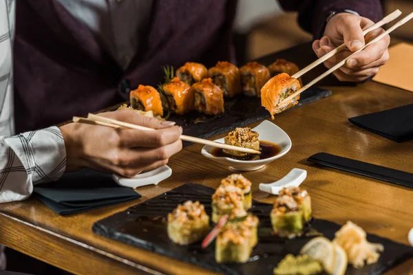 Vista recortada de la gente sumergiendo rollos de sushi en salsa de soja en el restaurante — Stock Photo