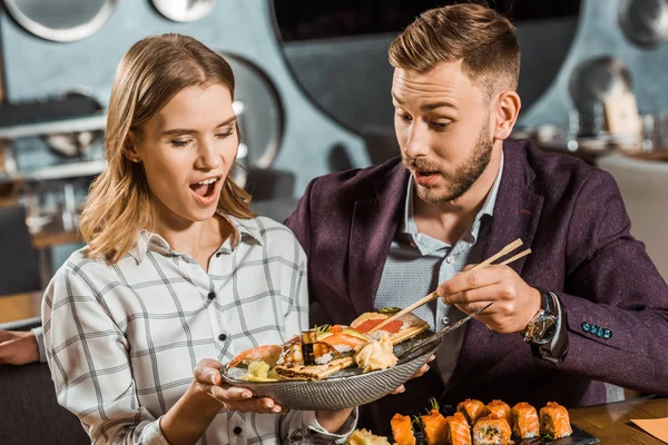 Surprised woman holding plate with seafood while couple having dinner in restaurant — Stock Photo