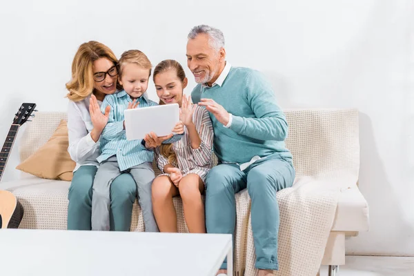Familia feliz saludando con las manos mientras tiene videollamada con tableta digital en casa - foto de stock