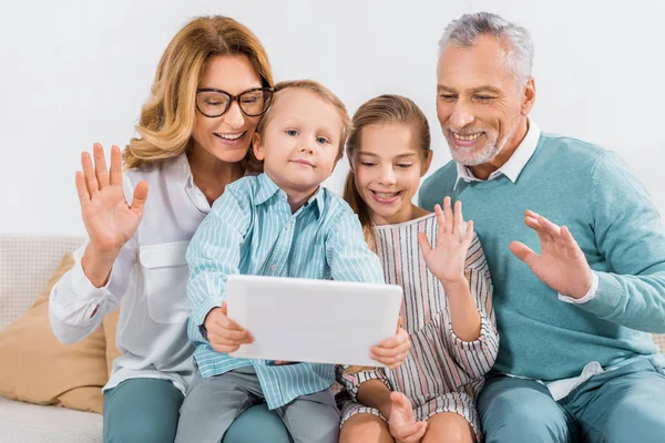 Niños y abuelos saludando con las manos mientras reciben videollamadas con tabletas digitales en casa - foto de stock
