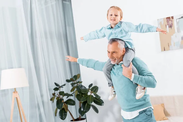 Adorable little kid sitting on grandfather shoulders and having fun at home — Stock Photo