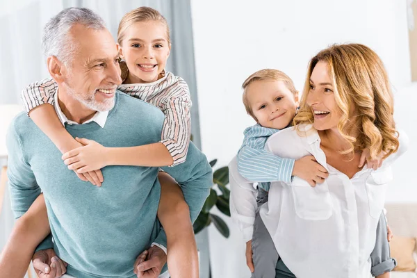 Lachende Großeltern machen Huckepackfahrt zu entzückenden Enkeln zu Hause — Stockfoto