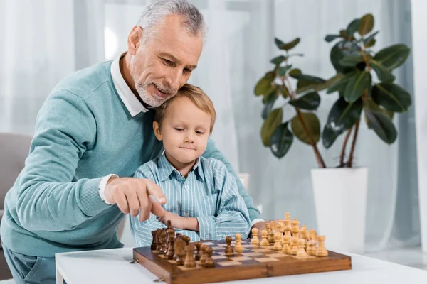 Cheerful middle aged man playing chess with adorable grandson at home — Stock Photo