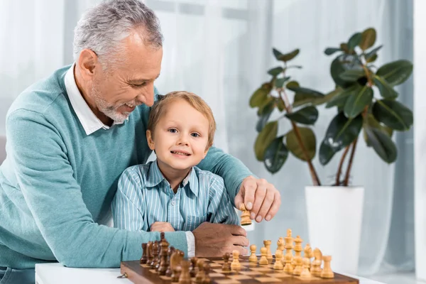 Positive mature man playing chess with adorable grandson at home — Stock Photo