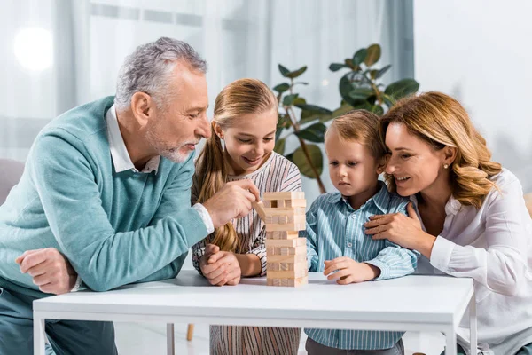 Cheerful grandparents and grandchildren playing blocks wood tower game together at home — Stock Photo