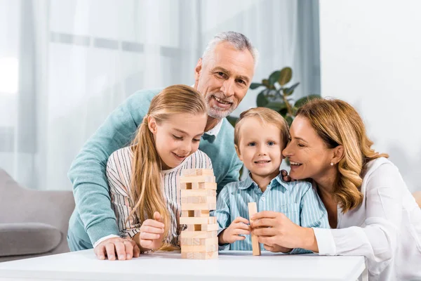 Foyer sélectif de grands-parents et petits-enfants jouant blocs tour de bois jeu ensemble à la maison — Photo de stock