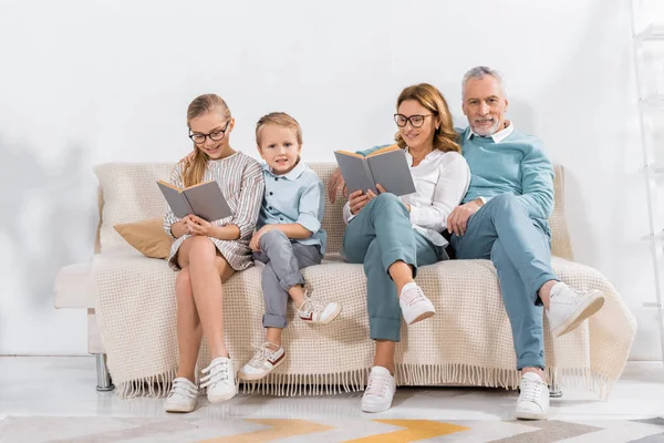Grandchildren and grandparents reading books on sofa at home — Stock Photo