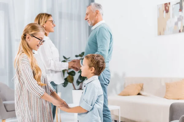 Vue latérale du couple mature se tenant la main l'un de l'autre et de leurs petits-enfants se tenant la main près de chez eux — Photo de stock