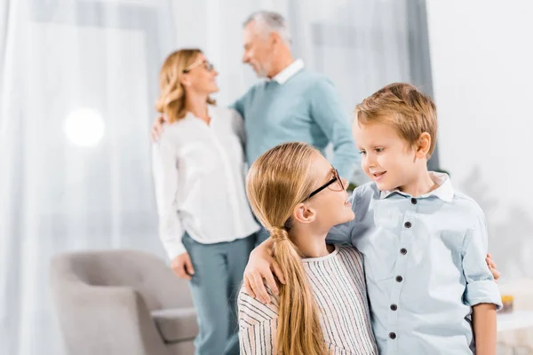 Adorable kids looking at each other and embracing while their grandparents standing behind at home — Stock Photo