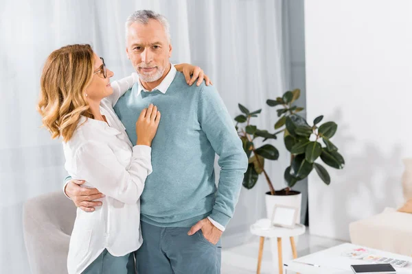 Smiling middle aged couple embracing each other in living room at home — Stock Photo