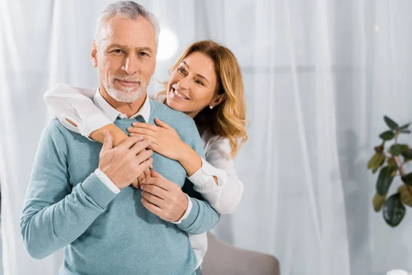 Happy wife embracing mature husband from behind at home — Stock Photo