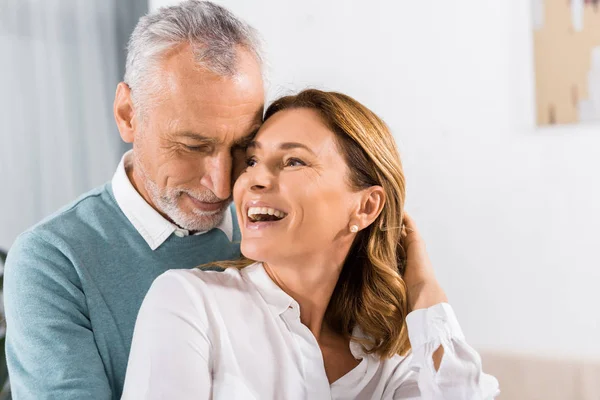 Primer plano vista de guapo de mediana edad hombre abrazando riendo mujer en casa - foto de stock