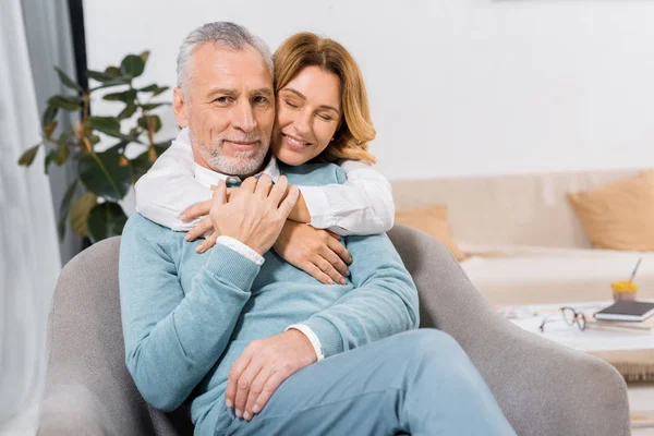 Atractiva mujer con los ojos cerrados abrazando marido de mediana edad en casa - foto de stock