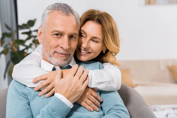 Enfoque selectivo de la mujer atractiva feliz abrazando marido de mediana edad en casa - foto de stock