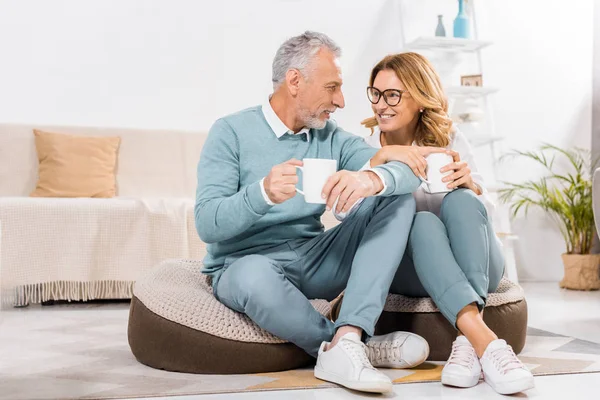 Pareja de mediana edad sentado con tazas de café en la sala de estar en casa - foto de stock