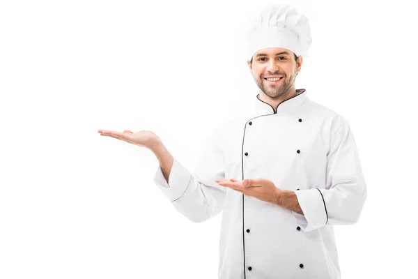 Glücklicher junger Koch, der auf Leerstellen zeigt und isoliert auf weiße Kamera schaut — Stockfoto