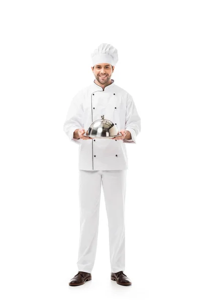 Красивый молодой шеф-повар держит подающий поднос с куполом и смотрит на камеру, изолированную на белом — стоковое фото