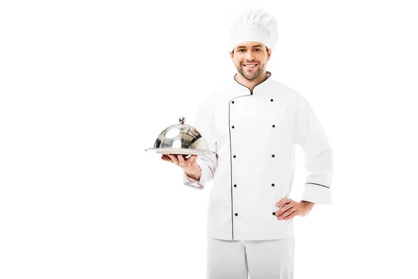 Junger Koch hält Servierteller mit Kuppel und blickt isoliert in die Kamera auf weiß — Stockfoto