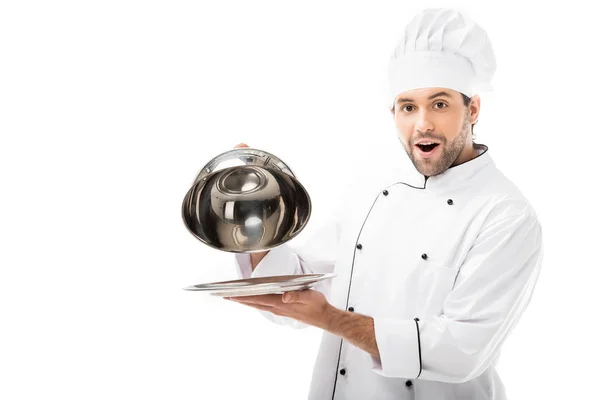 Excited young chef taking of serving dome from plate and looking at camera isolated on white — Stock Photo