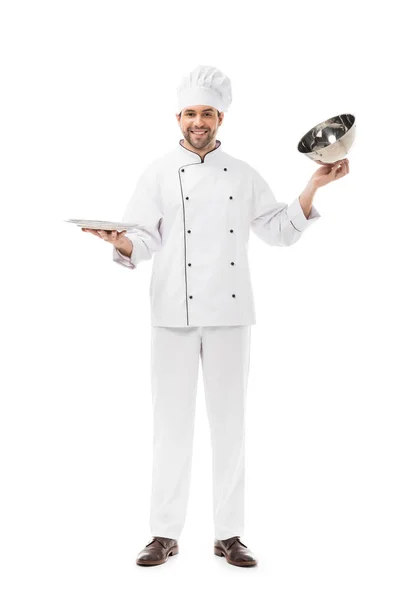 Улыбающийся молодой шеф-повар берет подающий купол с тарелки и смотрит на камеру, изолированную на белом — стоковое фото