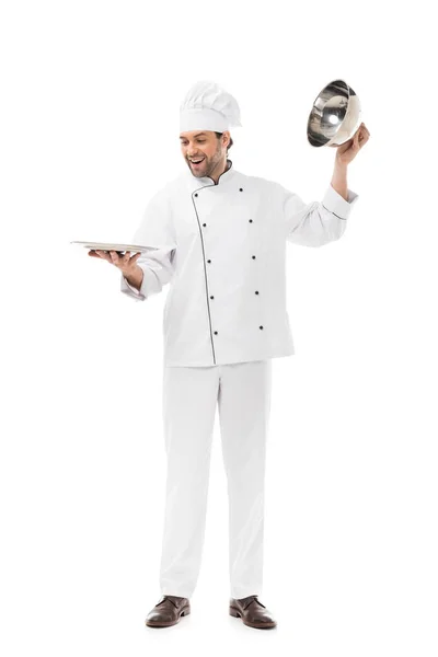 Happy young chef taking of serving dome from plate isolated on white — Stock Photo