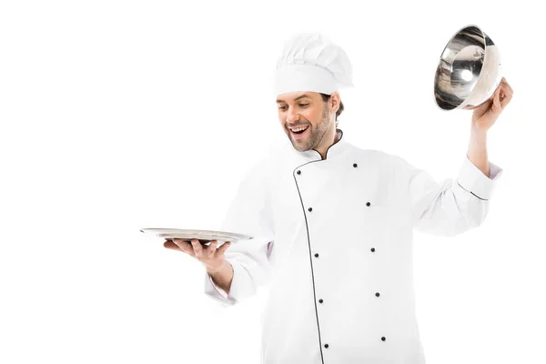Glücklicher junger Koch, der die Servierkuppel vom Teller nimmt, isoliert auf weiß — Stockfoto