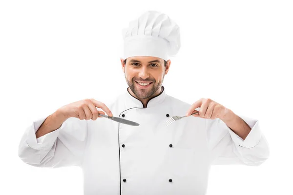 Felice giovane chef tenendo forchetta e coltello e guardando la fotocamera isolata su bianco — Foto stock