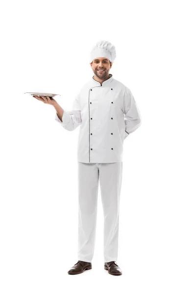 Feliz joven chef sosteniendo plato vacío y mirando a la cámara aislada en blanco - foto de stock