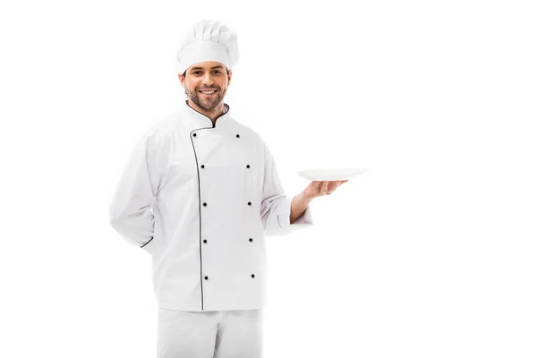 Guapo joven chef sosteniendo plato vacío y mirando a la cámara aislada en blanco - foto de stock