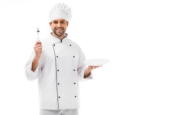 Giovane chef sorridente con piatto e forchetta guardando telecamera isolata su bianco — Foto stock