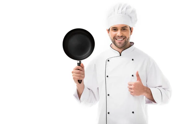 Feliz joven chef sosteniendo sartén y mostrando el pulgar hacia arriba aislado en blanco — Stock Photo