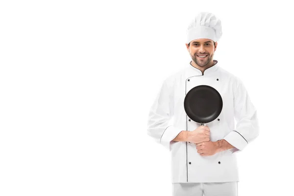 Happy young chef holding frying pan and looking at camera isolated on white — Stock Photo