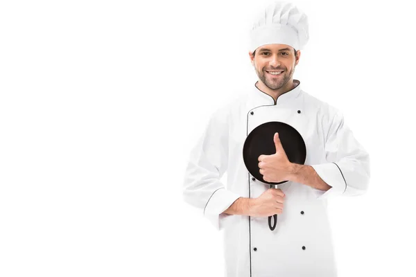 Sonriente joven chef sosteniendo sartén y mostrando el pulgar hacia arriba aislado en blanco - foto de stock