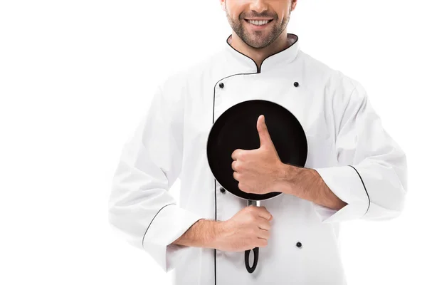 Обрізаний знімок усміхненого молодого шеф-кухаря, що тримає сковороду і показує великий палець вгору ізольовано на білому — стокове фото