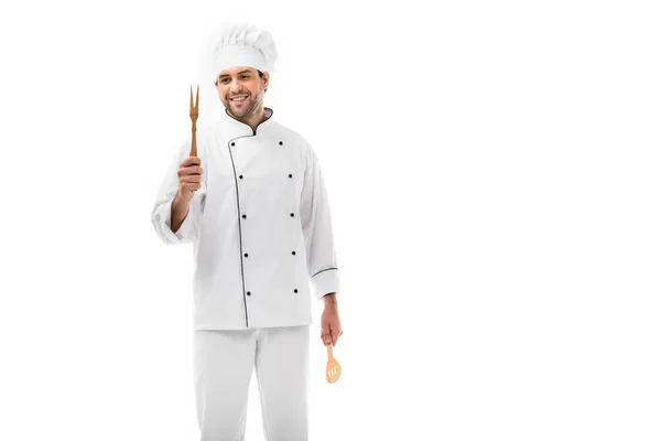 Sonriente joven chef sosteniendo utensilios de cocina de madera aislados en blanco - foto de stock