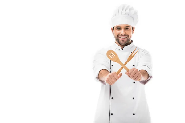 Sorrindo jovem chef segurando utensílios de cozinha de madeira e olhando para a câmera isolada no branco — Fotografia de Stock